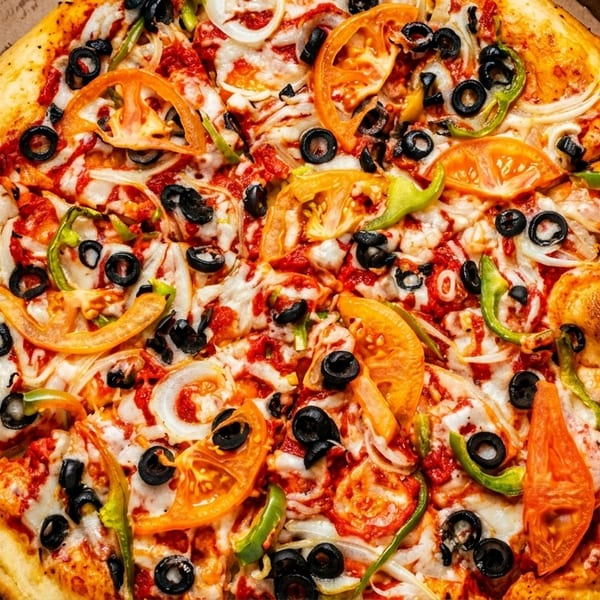A freshly baked pizza with tomatoes, onions, olives, and green peppers in a cardboard box.