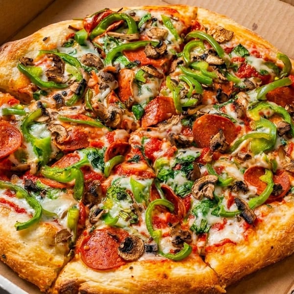 A whole pepperoni, mushroom, and green pepper pizza sits in an open cardboard delivery box.