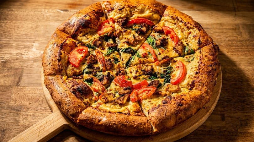 A freshly baked pizza with tomatoes, spinach, and chicken on a wooden serving board.
