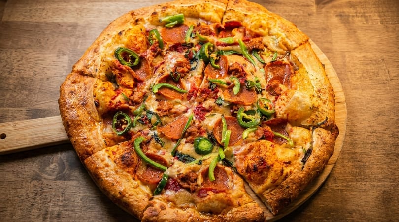 A freshly baked pizza with pepperoni, sausage, and green peppers on a wooden peel.