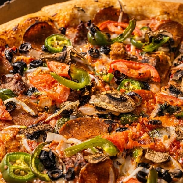 Close-up of a supreme pizza with pepperoni, sausage, olives, mushrooms, peppers, and tomatoes.